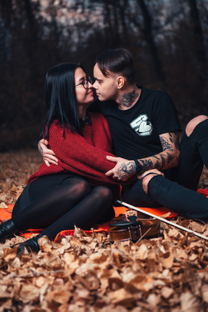young man and young woman are sitting on a plaid in an autumn forest.の写真素材