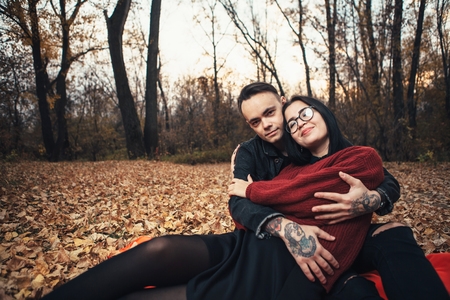 young man and young woman are sitting on a plaid in an autumn forest.の写真素材