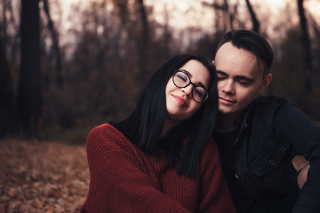 young man and young woman are sitting on a plaid in an autumn forest.の写真素材