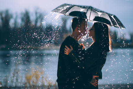 young couple standing under a dark umbrella.の写真素材