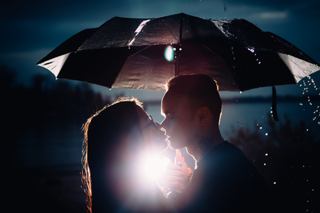 young man and woman under an umbrella and rain.の写真素材