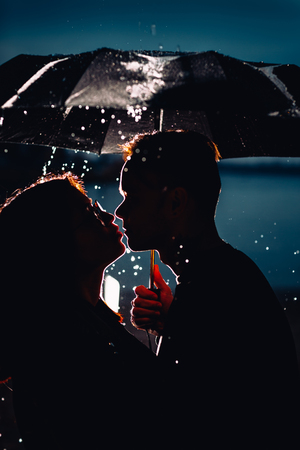 young man and woman under an umbrella and rain.の写真素材