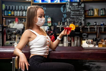 girls in medical masks drink cocktails.  girl in a medical mask is resting in a pub. girl in a medical mask in a pubの写真素材