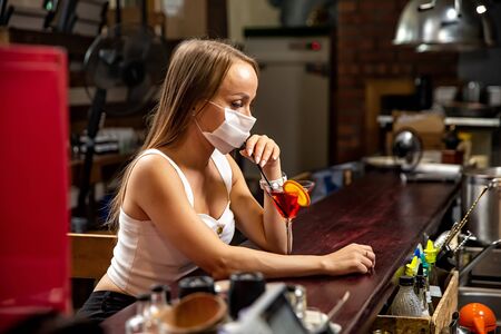 girls in medical masks drink cocktails.  girl in a medical mask is resting in a pub. girl in a medical mask in a pubの写真素材