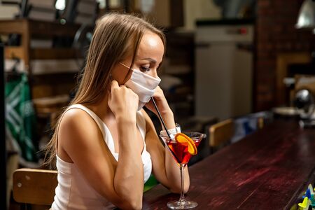 girls in medical masks drink cocktails.  girl in a medical mask is resting in a pub. girl in a medical mask in a pubの写真素材