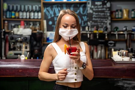 girls in medical masks drink cocktails.  girl in a medical mask is resting in a pub. girl in a medical mask in a pubの写真素材