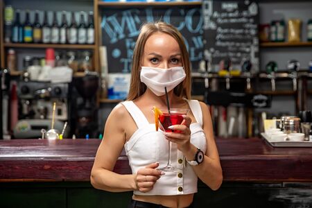 girls in medical masks drink cocktails.  girl in a medical mask is resting in a pub. girl in a medical mask in a pubの写真素材