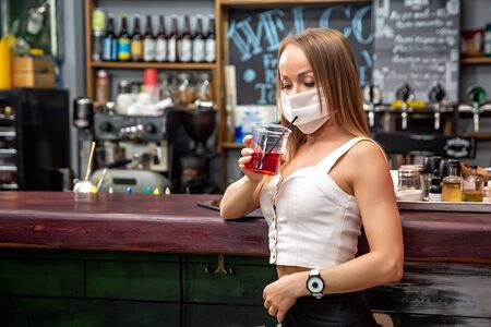 girls in medical masks drink cocktails.  girl in a medical mask is resting in a pub. girl in a medical mask in a pubの写真素材