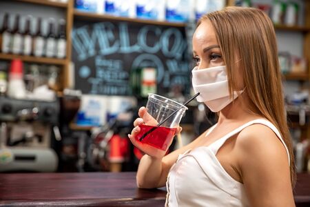 girls in medical masks drink cocktails.  girl in a medical mask is resting in a pub. girl in a medical mask in a pubの写真素材