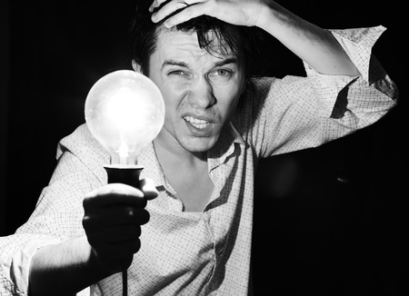 Man with electric bulb in the hand in the dark room. Black and white.の写真素材