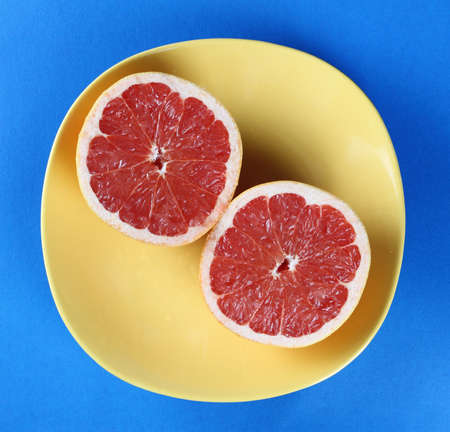 Red grapefruit on the yellow ceramic plate. Blue background.の写真素材