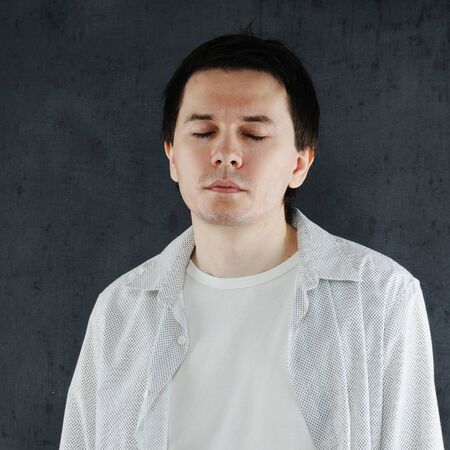 The man with the closed eyes is posing on the grey background.の写真素材