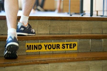 Man walking up the stairs with"Mind your step" safety caution sign about slips, trips and falls hazard.の写真素材