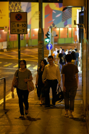 HONG KONG - September 4, 2017: People walking on warm lighted sidewalk at night. Street scene in Hong Kong.のeditorial素材