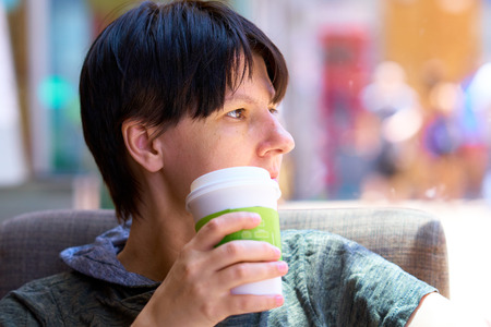 HONG KONG - July 1, 2018: Female tourist with with paper cup of hot coffee in hand looking out the window while sitting and relaxing in coffee shop.のeditorial素材