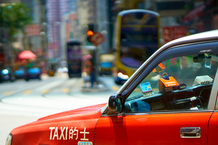HONG KONG - JULY 1, 2018: Red taxi cab with blurred cityscape in background. Public Transport in Hong Kong.のeditorial素材