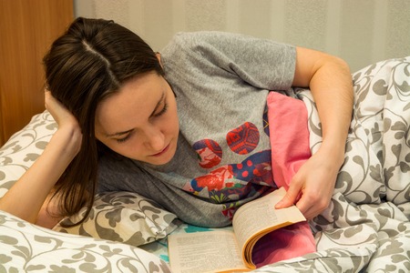 pretty girl reading book lying in bedの写真素材