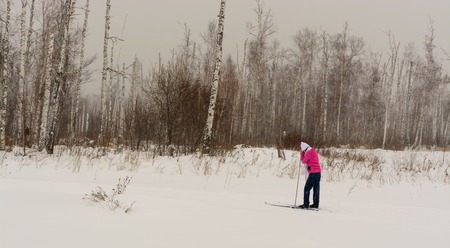 Tired girl standing on skis in winter forestの写真素材