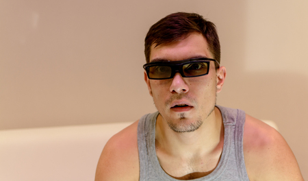 young man in 3D glasses at home on a white sofaの写真素材