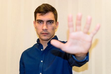 Young adult man making stop sign with his hand raised looking at cameraの写真素材