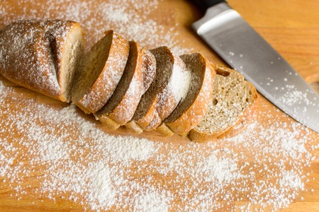 Fresh rye bread sliced on a wooden table with knifeの写真素材