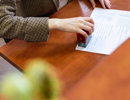 Female hand puts a seal on a document on an office deskの写真素材