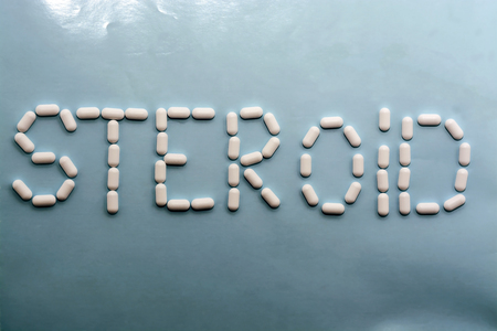 white pills on blue background. Word - steroidの写真素材
