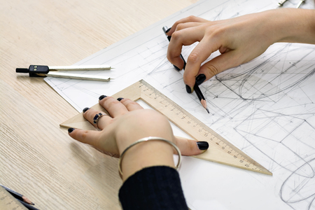 Girl architect draws a plan, graph, design, geometric shapes by pencil on large sheet of paper at...