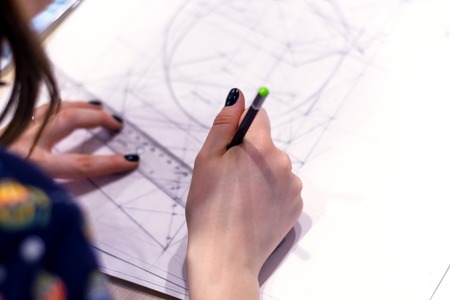 Girl architect draws a plan, graph, design, geometric shapes by pencil on large sheet of paper at office desk.の写真素材