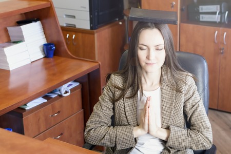 Young beautiful businesswoman meditates on the table in office. Attractive business lady using stress relief techniques at work.の写真素材
