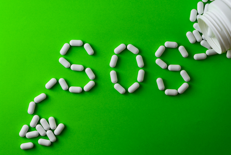 White pills on green background, which forming the word - SOS, with a blister of pills on...