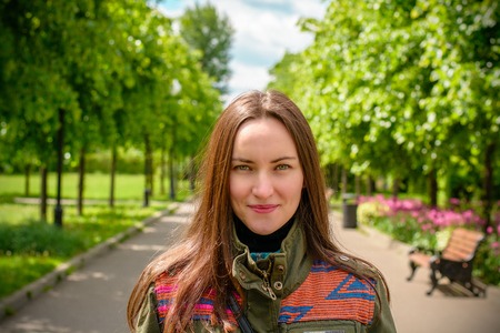 Beautiful young girl with long hair and in colored jacket in the summer park. The effect of...