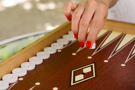 backgammon bone square white dice for gambling with blurred background. woman with red nails is playing backgammon.の写真素材