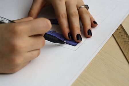 young woman - architect draws a plan, graphic, design, geometric shapes by pencil on large sheet of paper at office desk. crop image.の写真素材