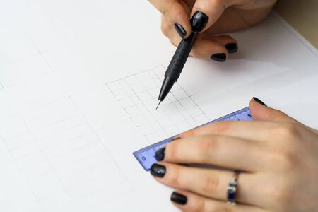 Girl student prepares a plan for student work at the University. Draws a black pencil and rulers on white paperの写真素材