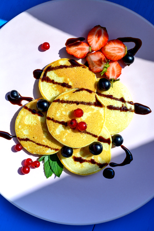 Ruddy pancake with currants, strawberries, mint, chocolate and ice cream on a pink plate in the bright rays of the morning sun. Healthy Breakfastの写真素材