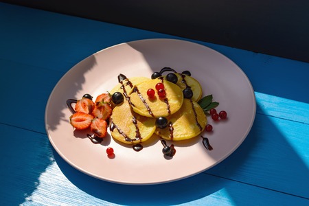 Ruddy pancake with currants, strawberries, mint, chocolate and ice cream on a pink plate in the bright rays of the morning sun. Healthy Breakfastの写真素材