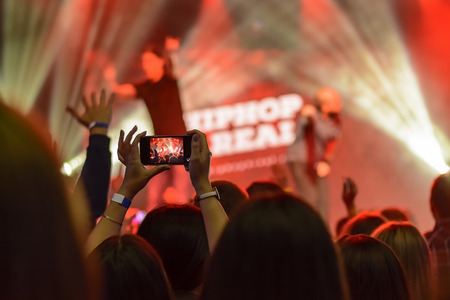 silhouette of hands with a smartphone on the background of the singing artists in the light of the red lightsの写真素材