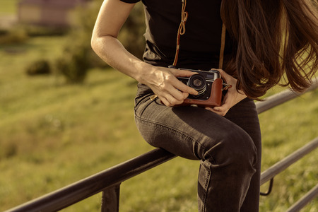 Young woman in black jeans and t-shirt, configures, retro film camera before shooting the autumn landscapeの写真素材