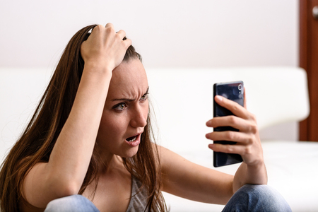 Young woman holding his head and looks to the smartphone. Distressed by what he saw. The concept of...