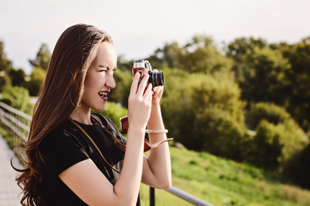 Cheerful young woman photographing scenery on a retro camera in autumn Park