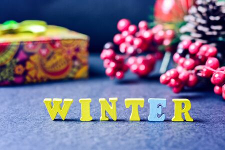 The word - Winter yellow wooden letters on a gray background with gifts, Christmas decorations, pine cones and a festive wreath. Concept - new yearの写真素材