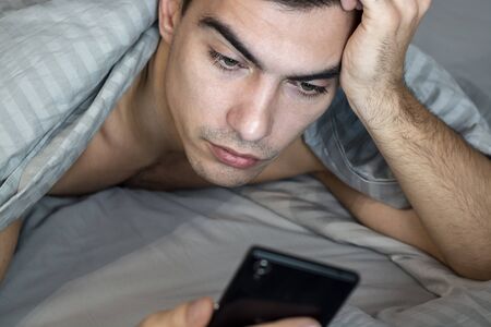 Close up portrait of happy young man messaging on smartphone in bed at home in morning. concept - social networking, technology, internet, communication and people.の写真素材