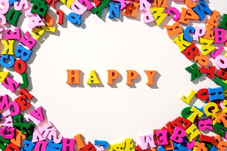 The word Happy is lined with colourful wooden letters on a white table with scattered in a circle with letters.の写真素材