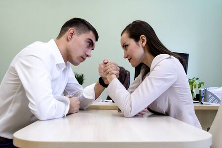 Man and woman in office clothes wrestling on hand at the Desk in the office.