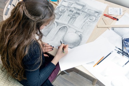Top view of the female architect designer draws sketches in pencil on white paper. Black and white drawing of an architectural elementの写真素材