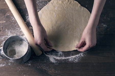 Women's hands roll out rolling pin dough on a wooden table, side light, Flatley, top viewの写真素材