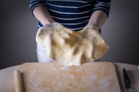 Women's hands throw rolled pizza dough into the air. front view, beginning of the dynamics