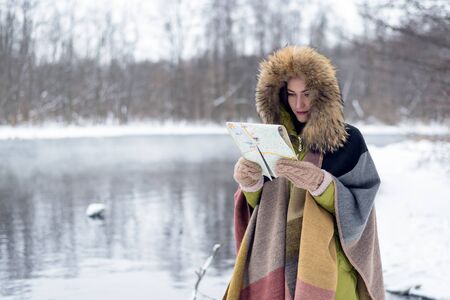 Portrait of a travelling woman in winter clothes standing in front of the lake in the winter forest with a map in the misty morning. Wanderlust. copy space.の写真素材