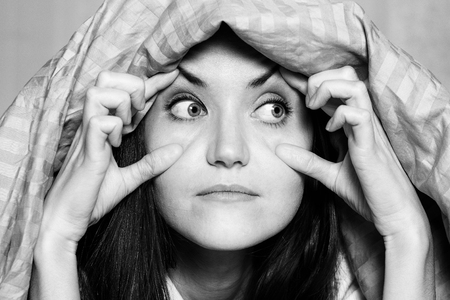 Black and white close-up portrait of a woman holding her eyes with her hands, suffering from...